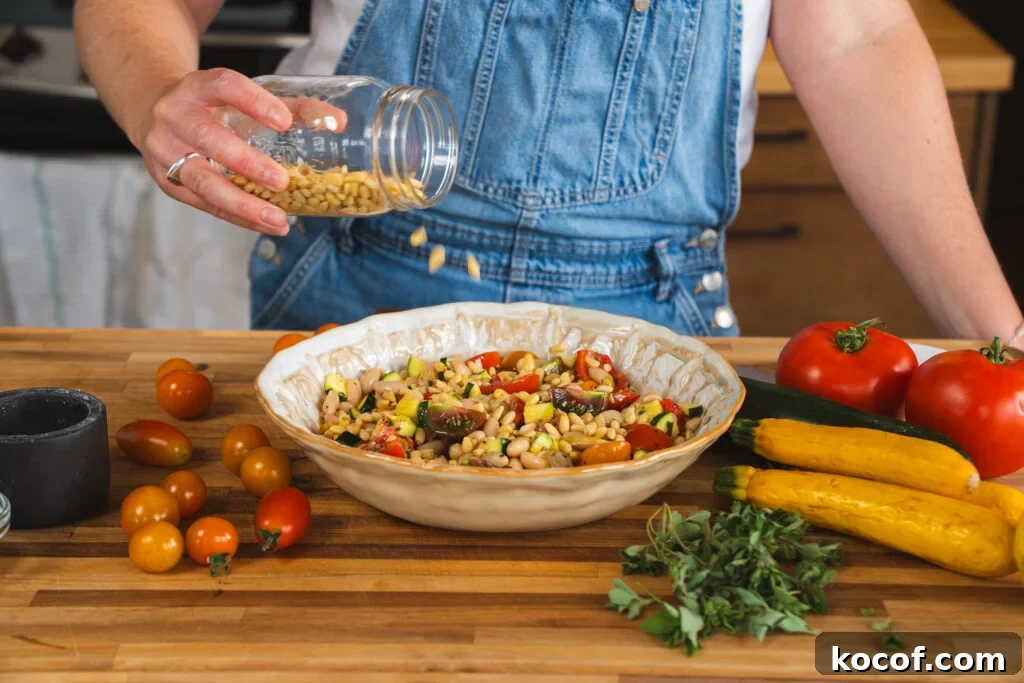 Pine nuts being added to a zucchini, tomato and white bean salad.