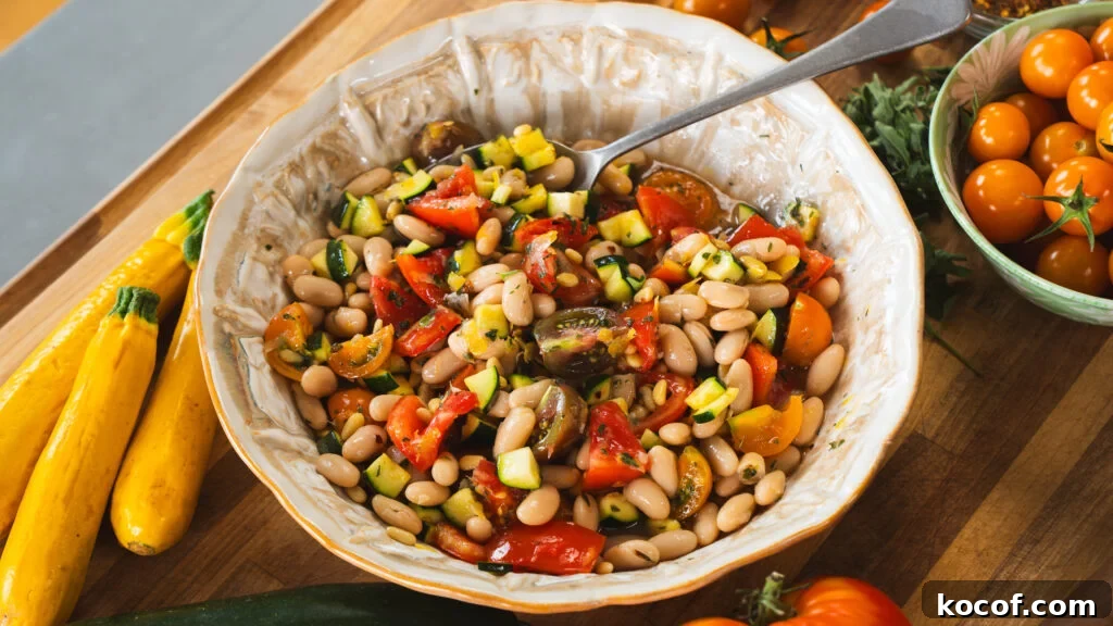 Zucchini, tomato and white bean salad in a large serving bowl with a spoon.