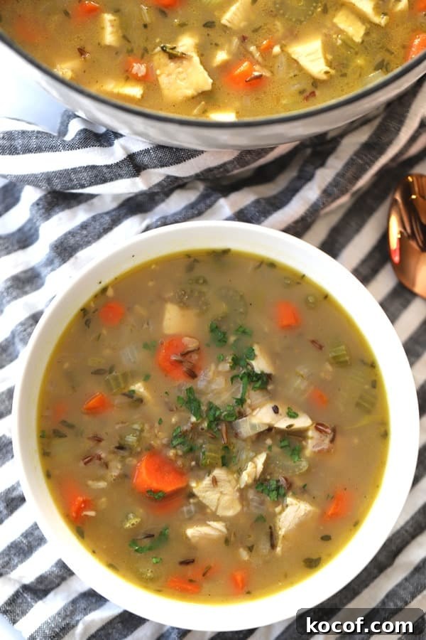 Turkey and wild rice soup in a white serving bowl with a large stock pot full of soup to the side.