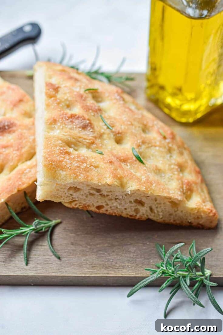 The sourdough focaccia is cut in half and on a wooden cutting board with an olive oil bottle in the background.