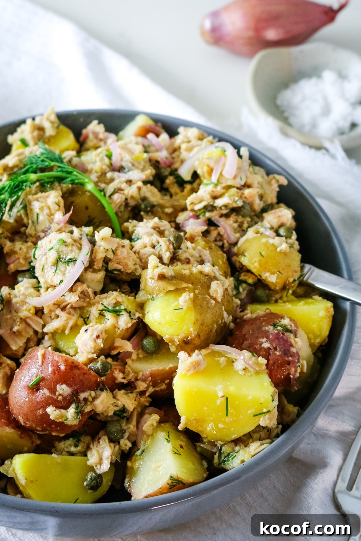 Lemon Dill Tuna & Potato Salad with Light Vinaigrette 2 A gray bowl filled with tuna potato salad, with salt and onion on the side.