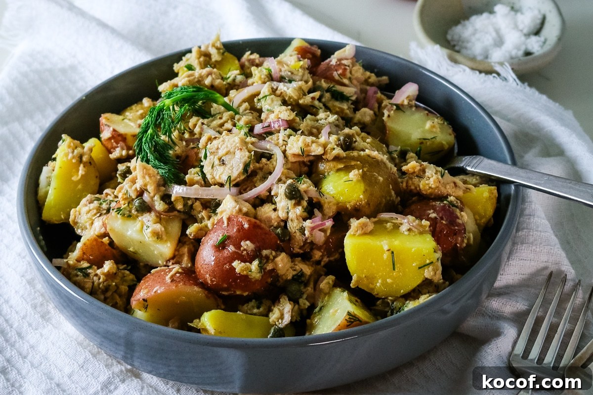 Lemon Dill Tuna & Potato Salad with Light Vinaigrette 11 A gray bowl filled with tuna potato salad, with a spoon inside, and salt on the side.