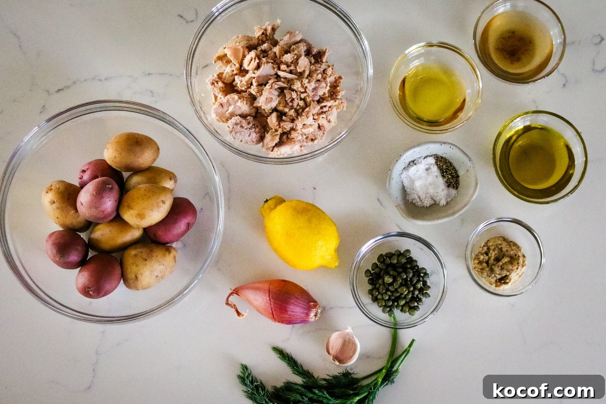 Lemon Dill Tuna & Potato Salad with Light Vinaigrette 4 Potatoes, tuna, and seasonings in a glass bowl, with lemon, onion, a clove of garlic, and herbs on the table.