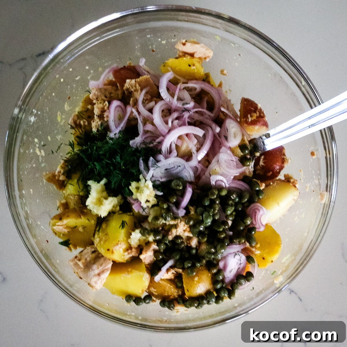 Lemon Dill Tuna & Potato Salad with Light Vinaigrette 10 A clear bowl filled with a mix of tuna, potato, onion, herbs, and seasoning.