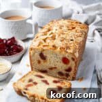 Vegan cherry loaf cake on a marble board with cups of tea and bowls of glace cherries and flaked almonds.