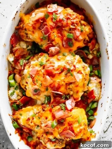 three baked chicken breasts in a white baking dish, topped with melted cheese, crumbled bacon, and sliced green onions.