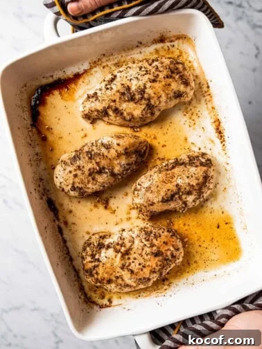 Hands holding baked chicken breasts in baking dish