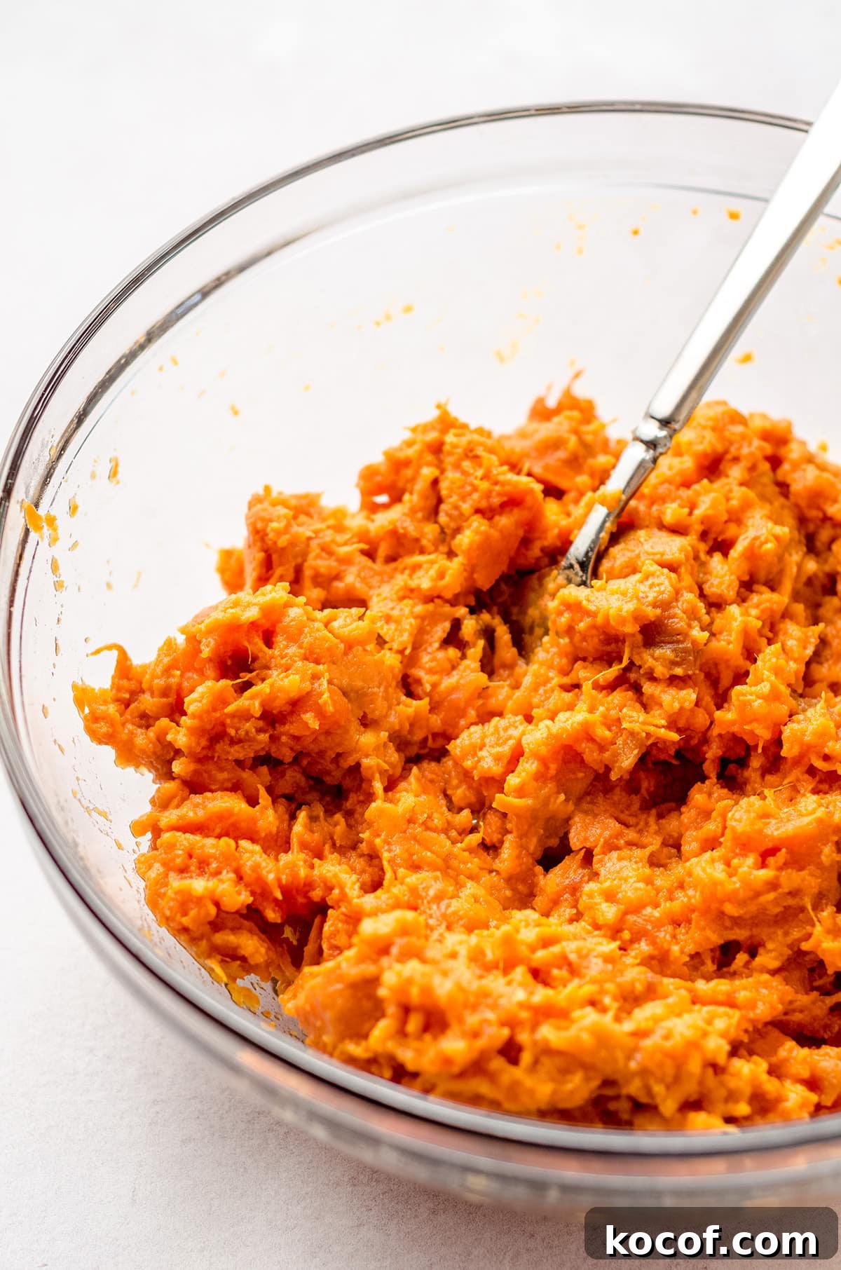 Mashing cooked sweet potato with a fork until well broken down.