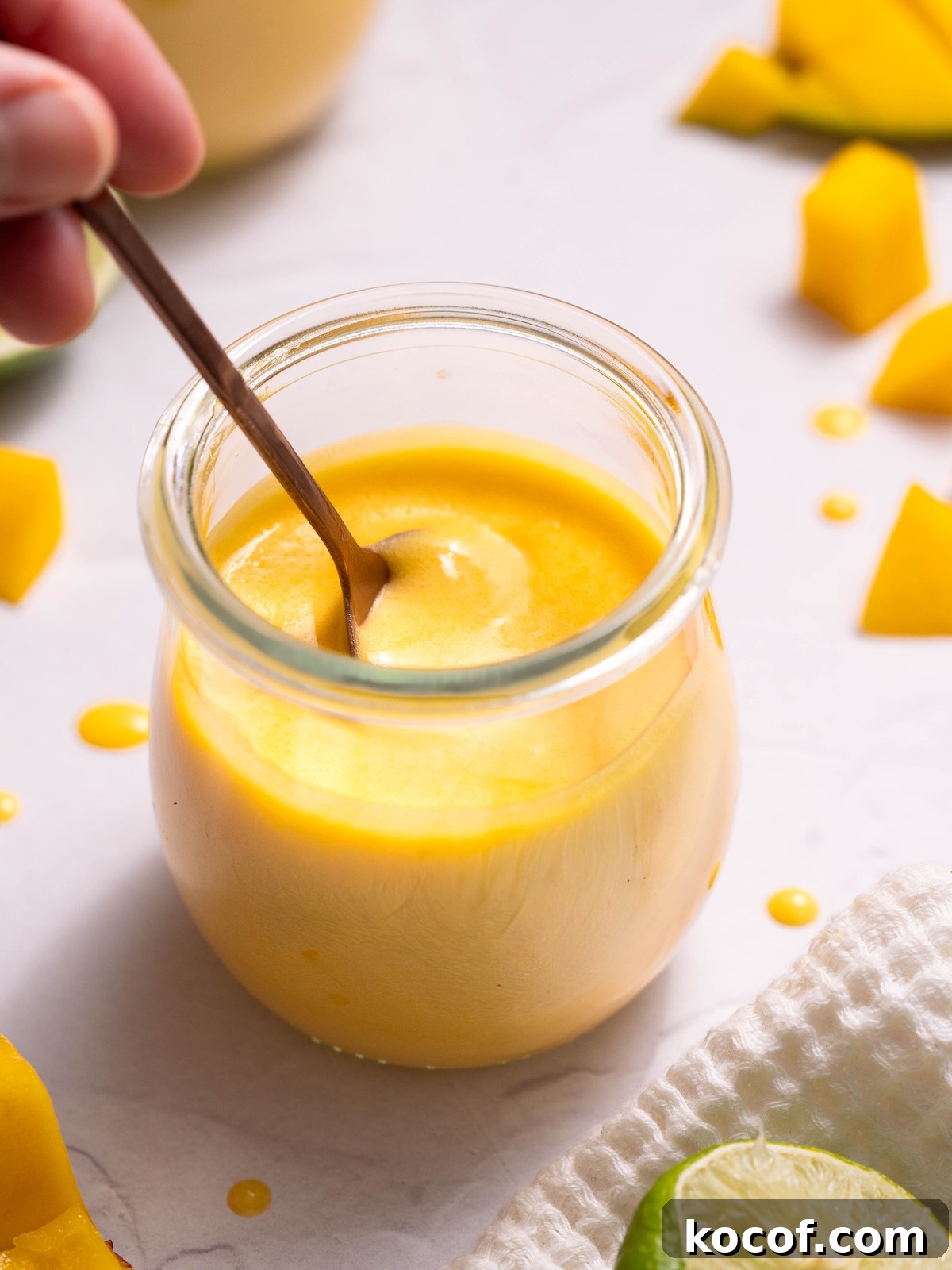 Dipping a copper spoon into a jar of fresh mango curd