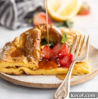 A picture of a slice of a German pancake on a plate topped with strawberries