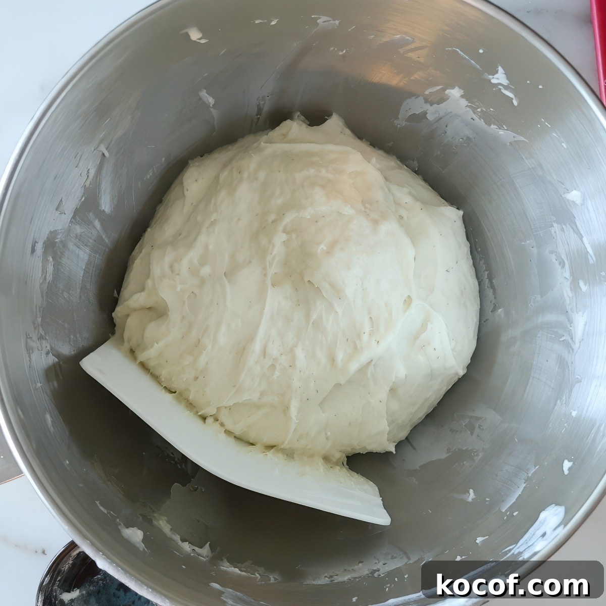 dough in stainless steel bowl with white bowl scraper.