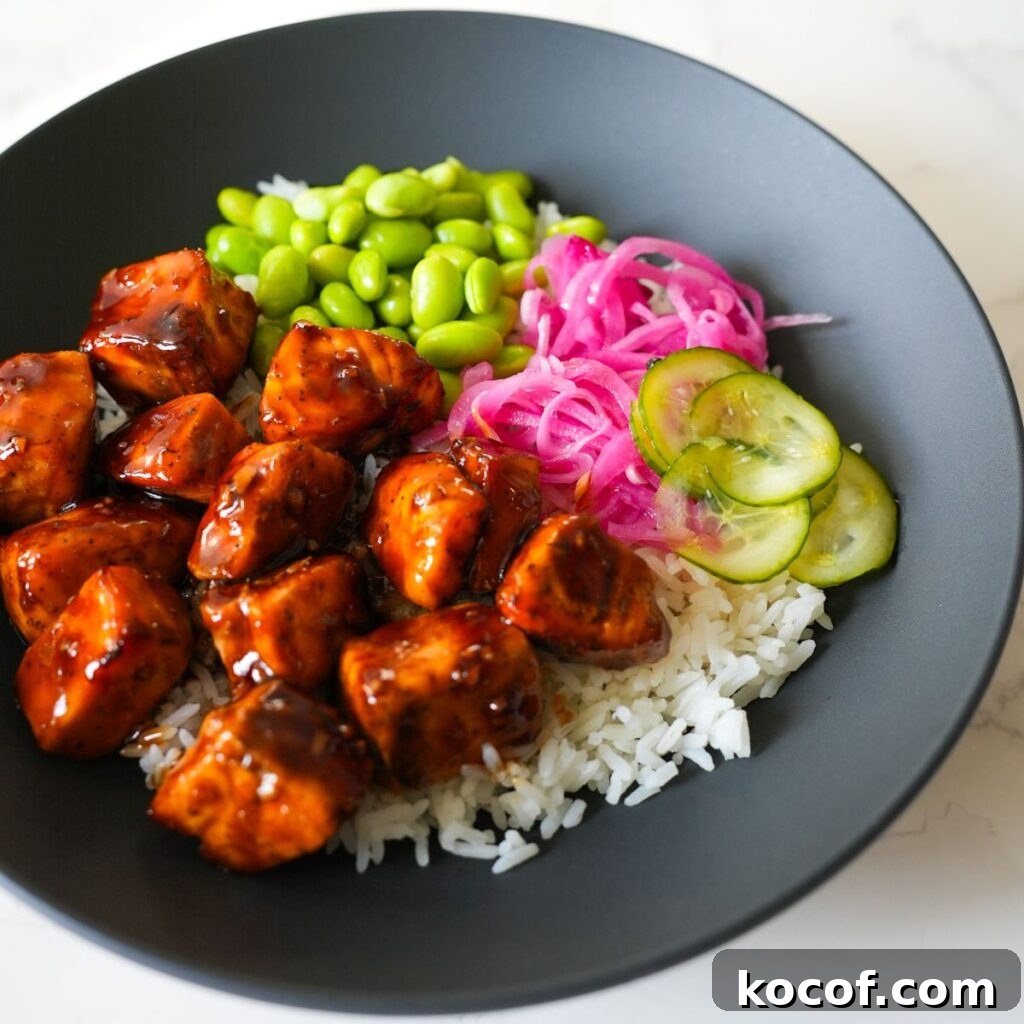 Teriyaki salmon on top of rice with pickled cucumber and onions in a black bowl.