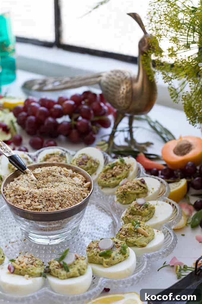 22 Delicious Easter Dinner Ideas That Aren’t Ham 2 Avocado deviled eggs on a deviled egg tray with a bunch of red grapes in the background and an metal peacock statue.