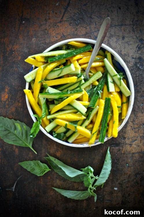 22 Delicious Easter Dinner Ideas That Aren’t Ham 11 An overhead image of strips of mango and cucumber in a dish with a spoon sticking out of one side and basil leaves sitting next to it.