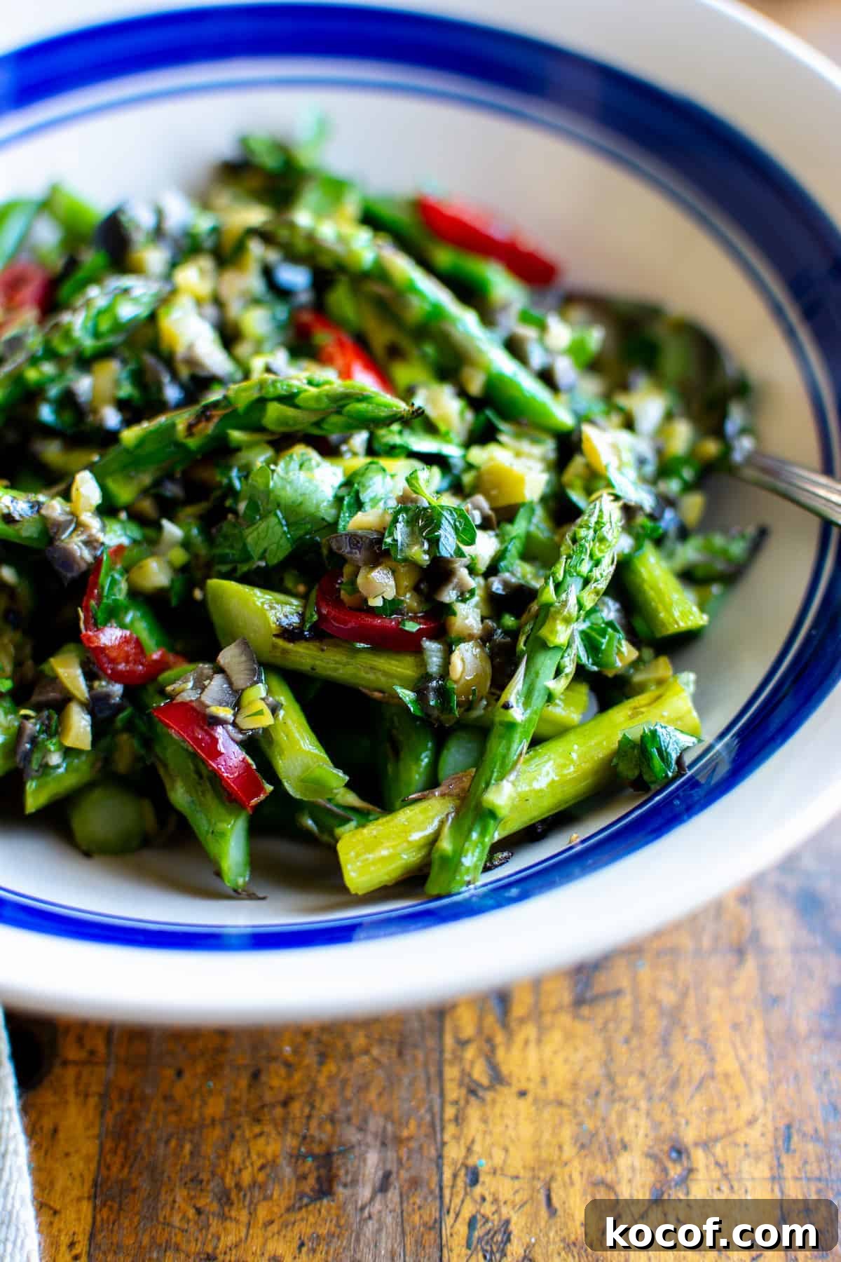 22 Delicious Easter Dinner Ideas That Aren’t Ham 13 A close up of an asparagus salad with olive dressing in a white bowl with a blue line around the edge and a spoon sticking in one side.