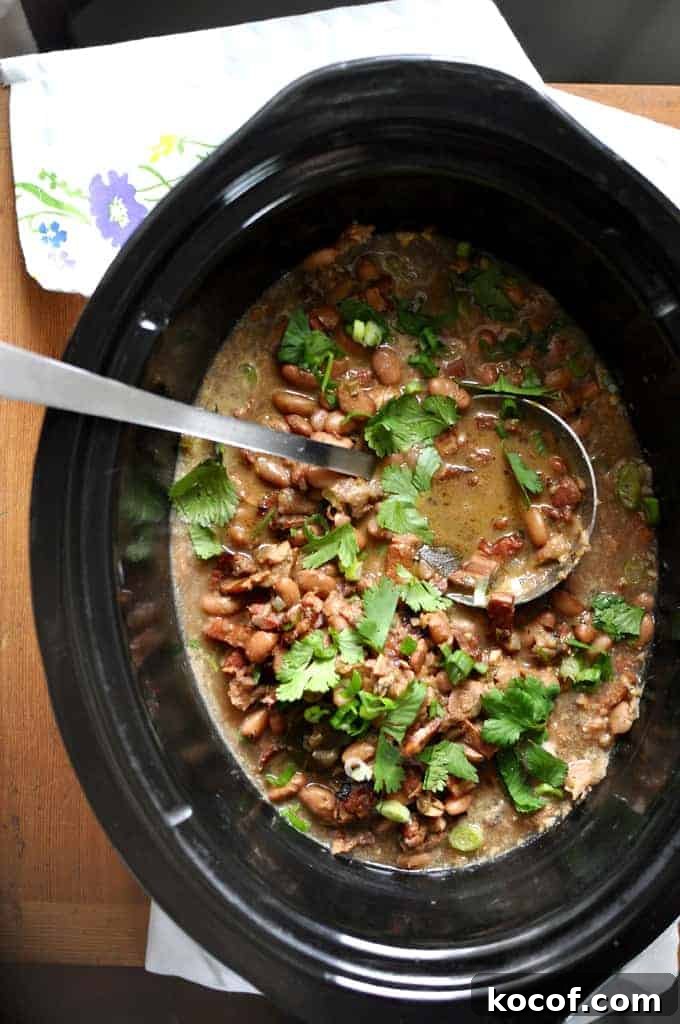 22 Delicious Easter Dinner Ideas That Aren’t Ham 17 A black crock with pinto beans and cilantro on top with a ladle sticking out of one side.