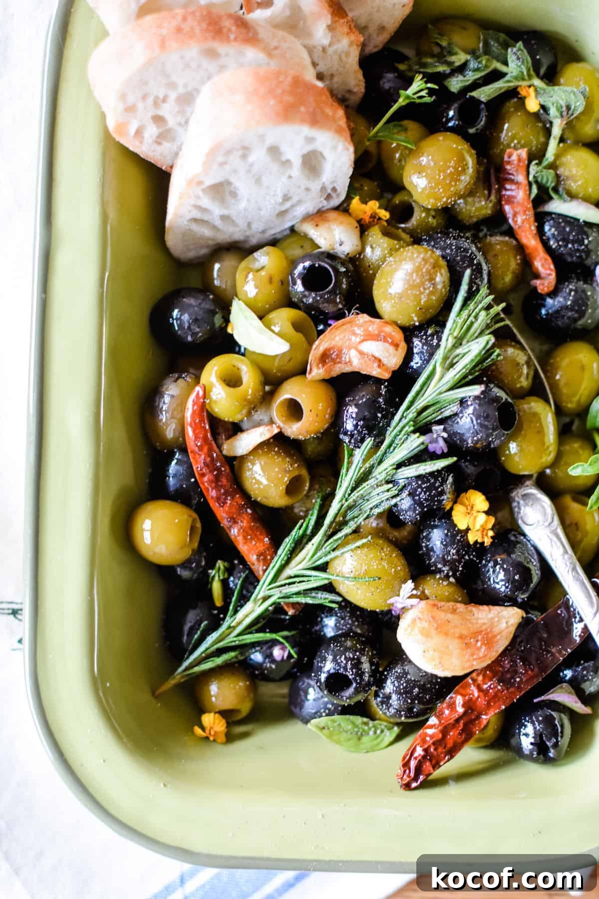 22 Delicious Easter Dinner Ideas That Aren’t Ham 4 A green dish with black and green olives in it and a sprig of rosemary on the top with roasted garlic and dried arbol chiles.