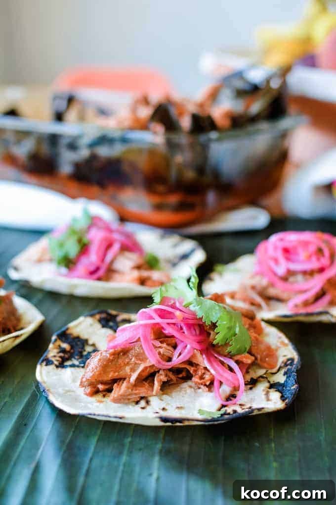 22 Delicious Easter Dinner Ideas That Aren’t Ham 8 Cochinita Pibil tacos with pickled red onions on top sitting on a banana leaf with a dish of cochinita behind it.