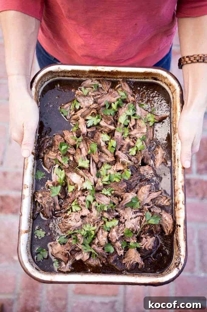 22 Delicious Easter Dinner Ideas That Aren’t Ham 9 A person in a pink shirt holding a dish of shredded beef barbacoa with cilantro leaves on top.