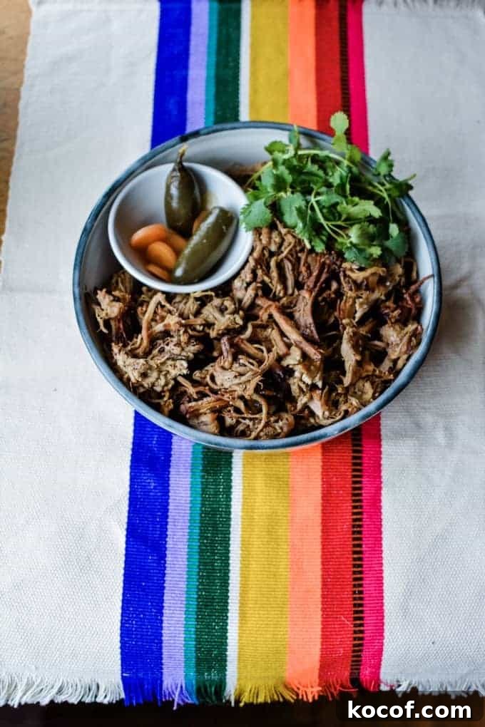 22 Delicious Easter Dinner Ideas That Aren’t Ham 10 A plate of carnitas on a rainbow table cloth with a dish of pickled jalapenos and a bunch of cilantro sitting next to it.