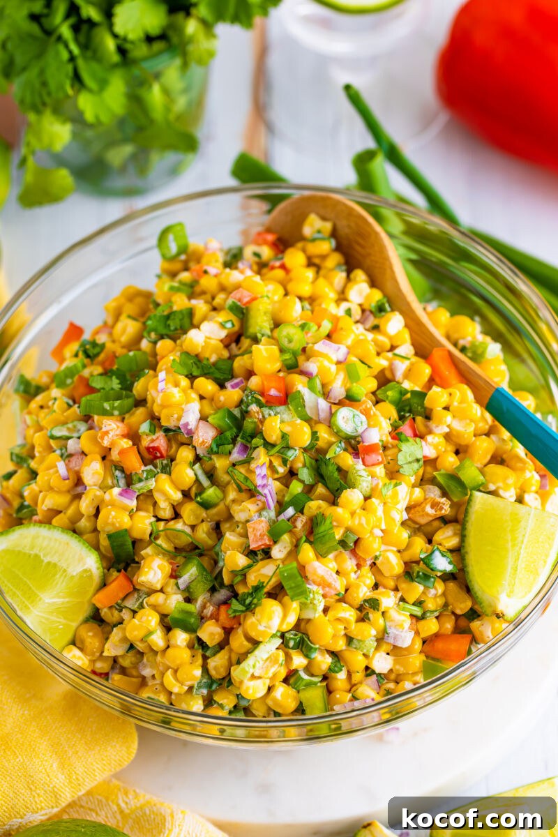 tex-mex corn salad in a glass serving bowl with lime wedges and a wooden spoon