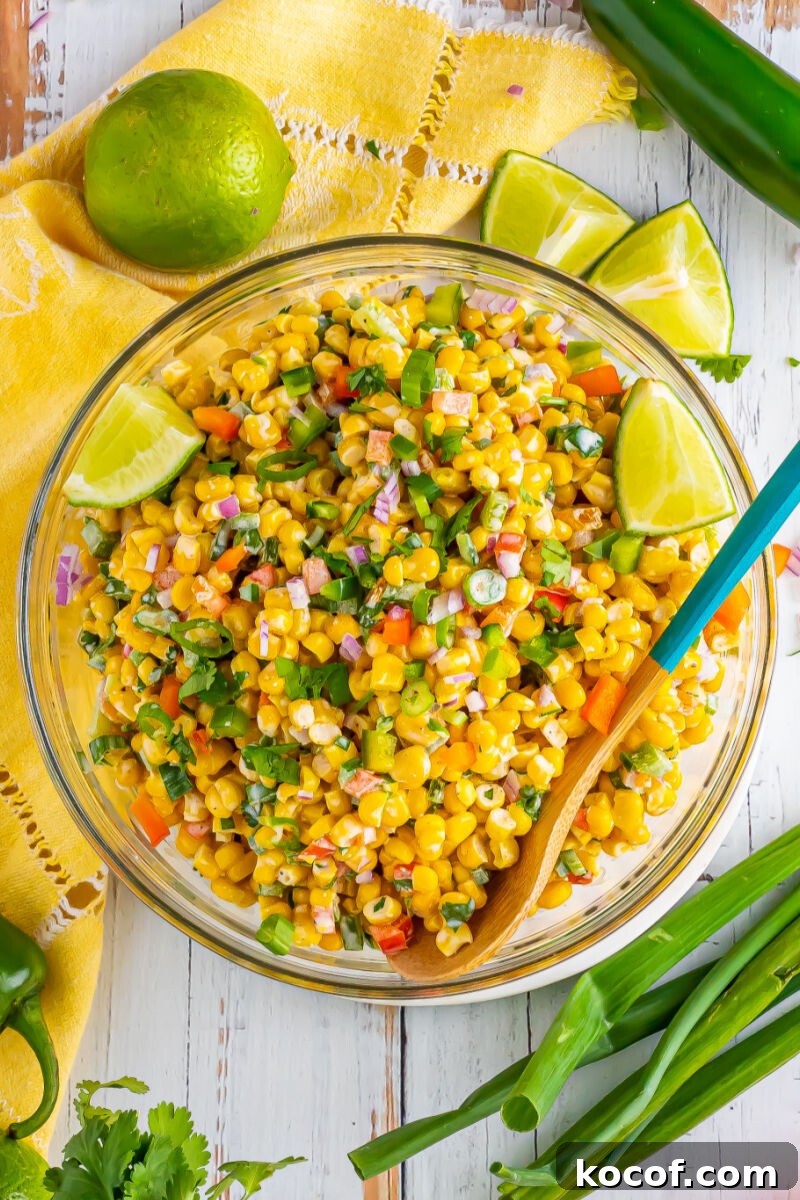 looking down at tex-mex corn salad in a serving bowl surrounded by limes and green onion