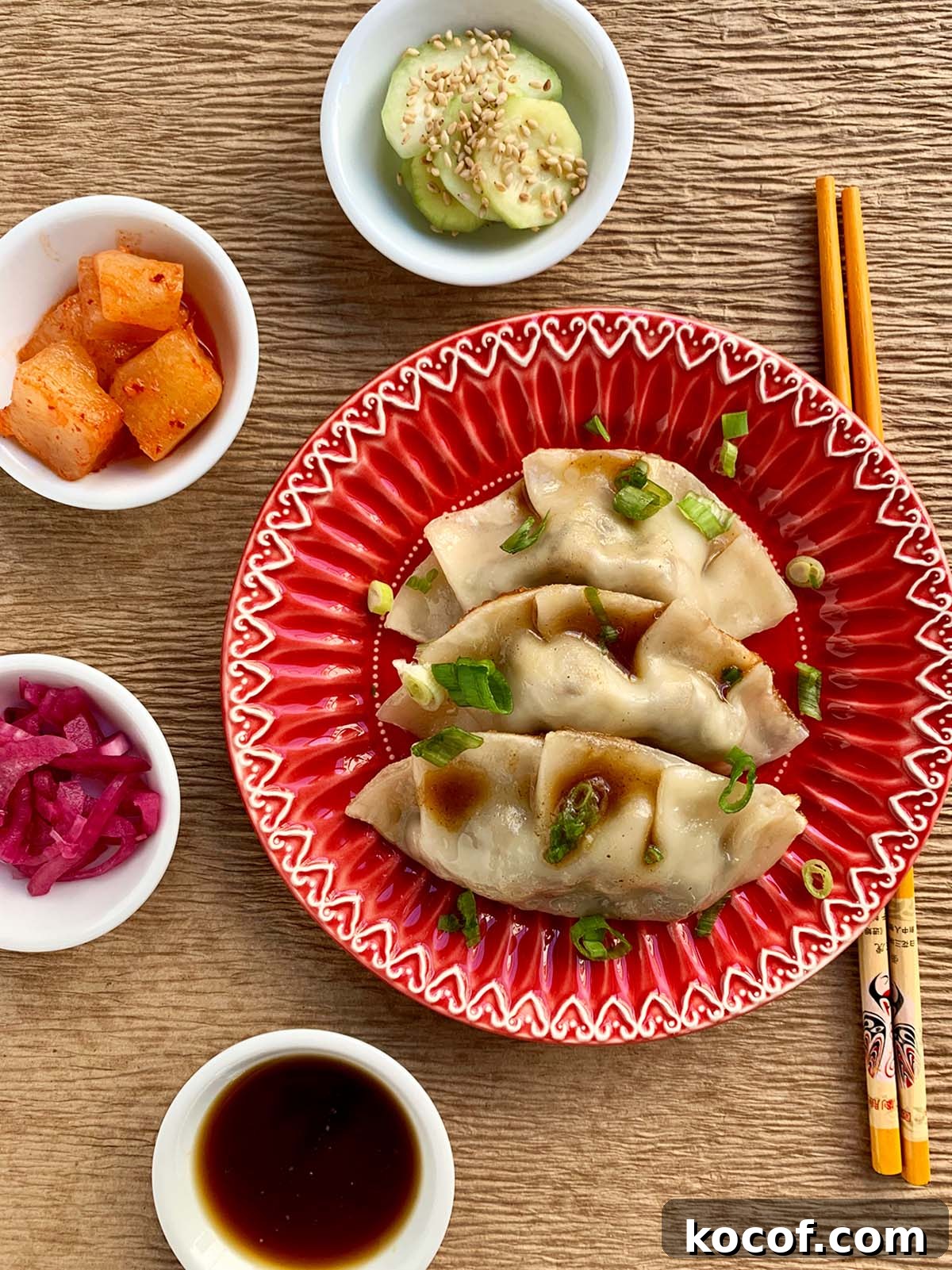 Korean Beef Mandu Dumplings Recipe: Authentic Jew Mandu Guide 2 Beef dumpling on a red plate with orange chopsticks and four small white bowls on the side.
