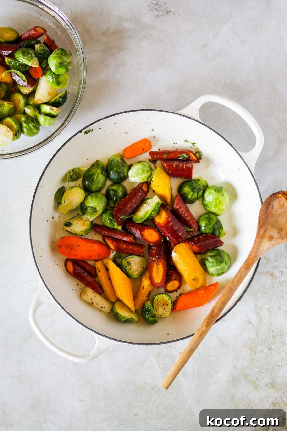 20 Delicious Side Dishes to Serve with Sliders 22 Brussel Sprouts and Carrots in a white Le Creuset braiser with a wooden spoon.