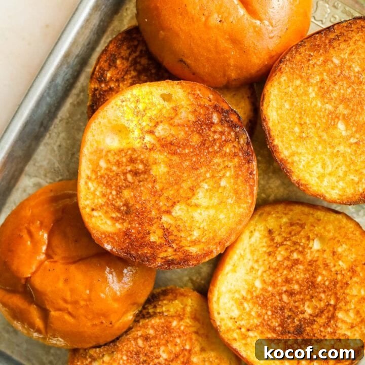 Up-close shot of golden toasted brioche burger buns on a baking sheet.