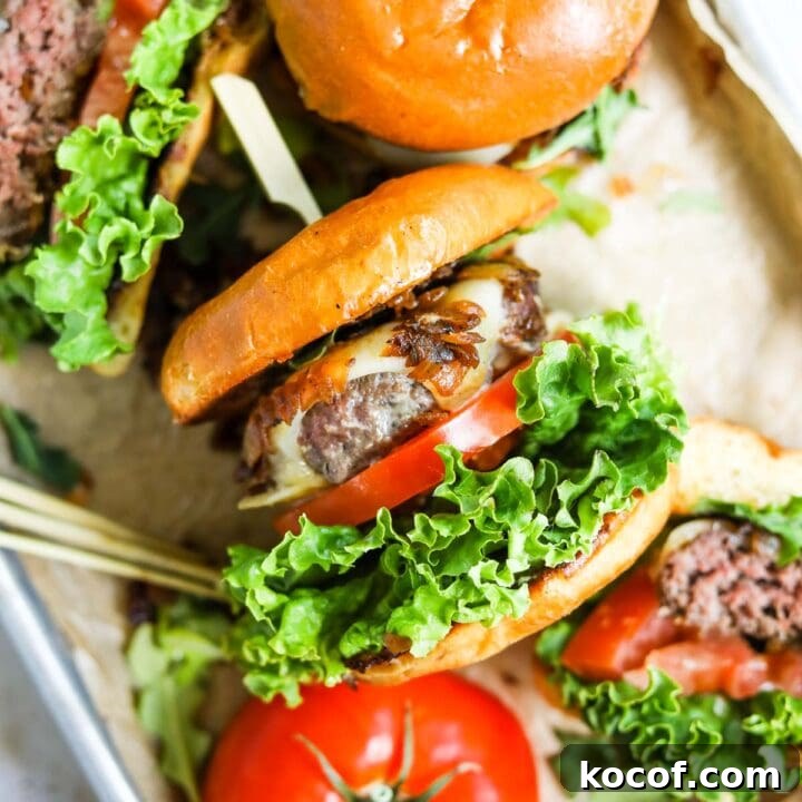 Cast iron skillet burger made on a stovetop in a baking sheet with other burgers and sliced tomato.