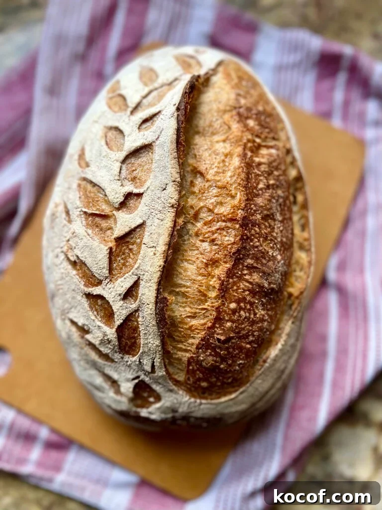 Baking Sourdough in a Loaf Pan: Step-by-Step Guide for Perfect Crust 3 An oval shaped loaf of artisan bread sits on a cutting board.