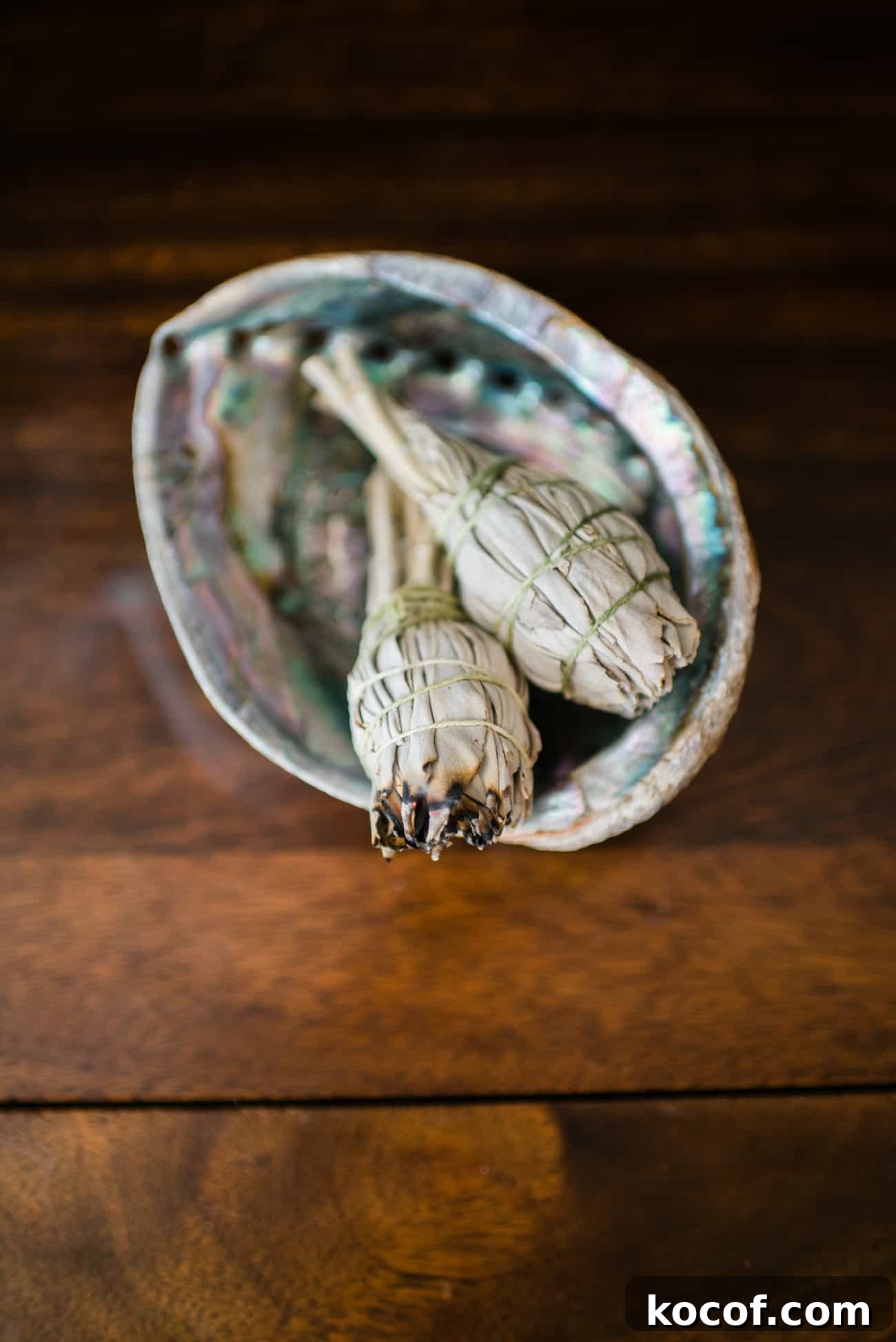 Smudge Your Home for Protection: Simple Ritual and Prayer 6 White sage smudge sticks in an abalone shell on a wooden table, used for a home cleansing ritual and smudging prayer.