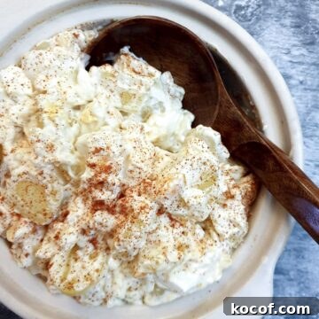 Creamy Potato and Egg Salad Recipe for Picnics & BBQs 9 A white serving dish of potato and egg salad with a wooden serving spoon.