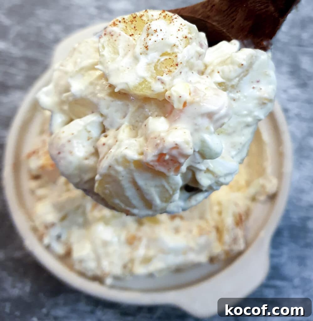 Creamy Potato and Egg Salad Recipe for Picnics & BBQs 3 A large spoonful of potato and egg salad held over a serving dish.