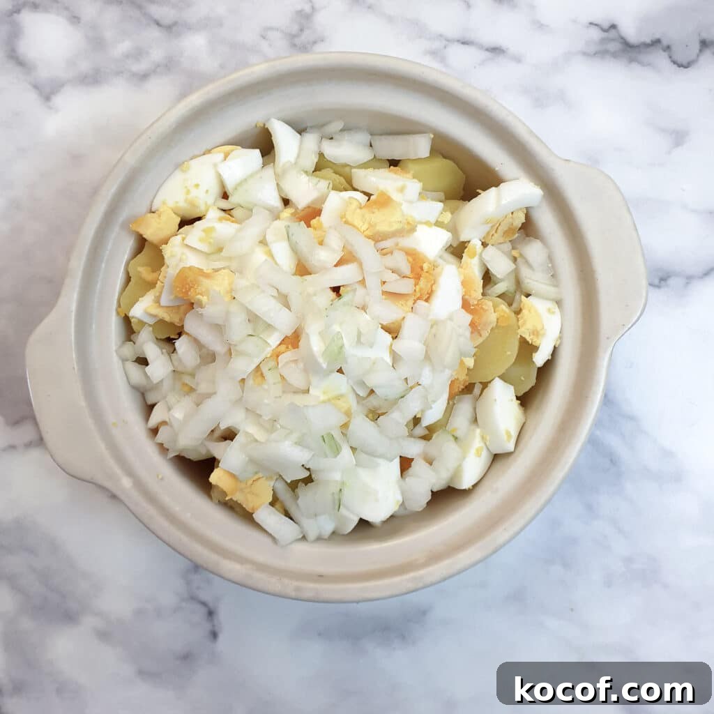 Creamy Potato and Egg Salad Recipe for Picnics & BBQs 6 Pieces of cooked potato, hard-boiled egg and chopped onion in a serving dish.