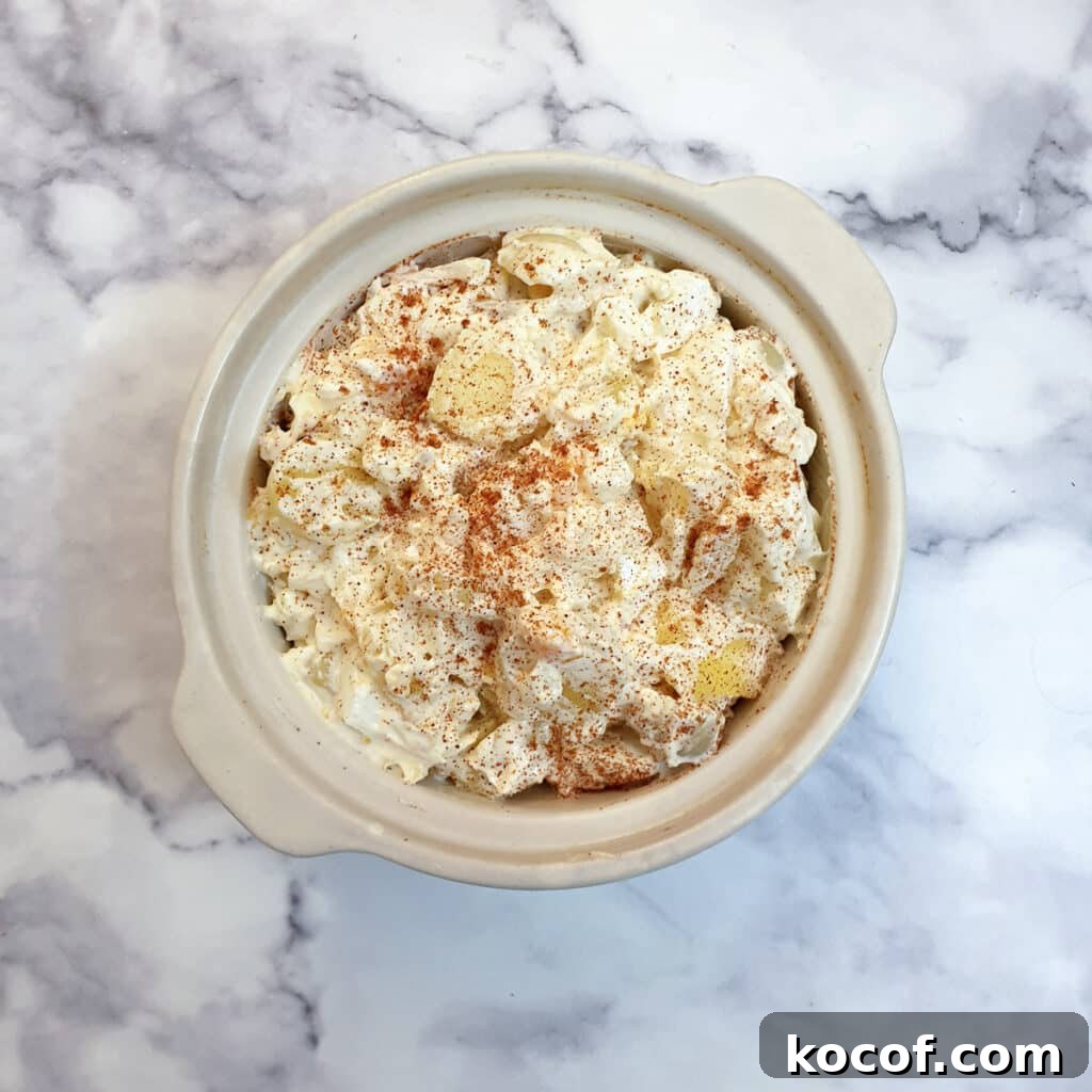 Creamy Potato and Egg Salad Recipe for Picnics & BBQs 7 Creamy egg and potato salad sprinkled with paprika in a white serving dish.
