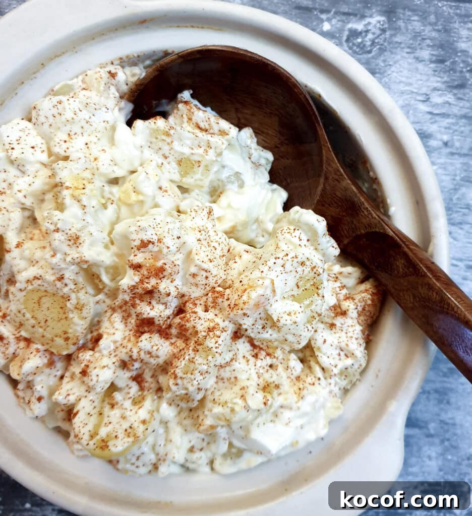 Creamy Potato and Egg Salad Recipe for Picnics & BBQs 8 A white serving dish of potato and egg salad with a wooden serving spoon.