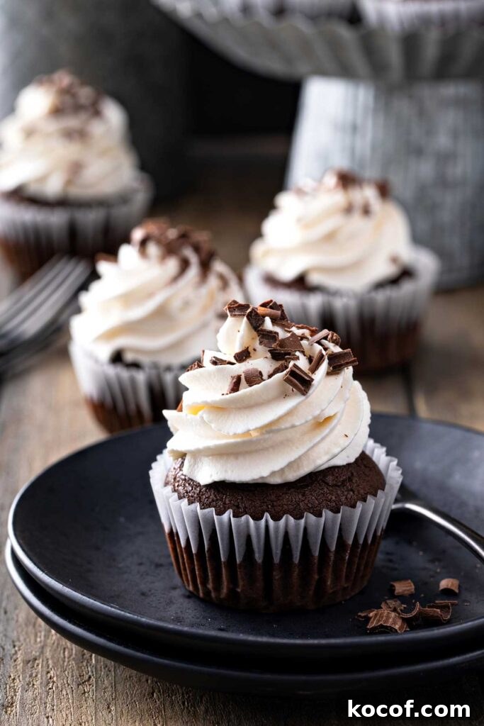 Chocolate cupcake with whipped frosting and chocolate shavings on a black dessert plate.