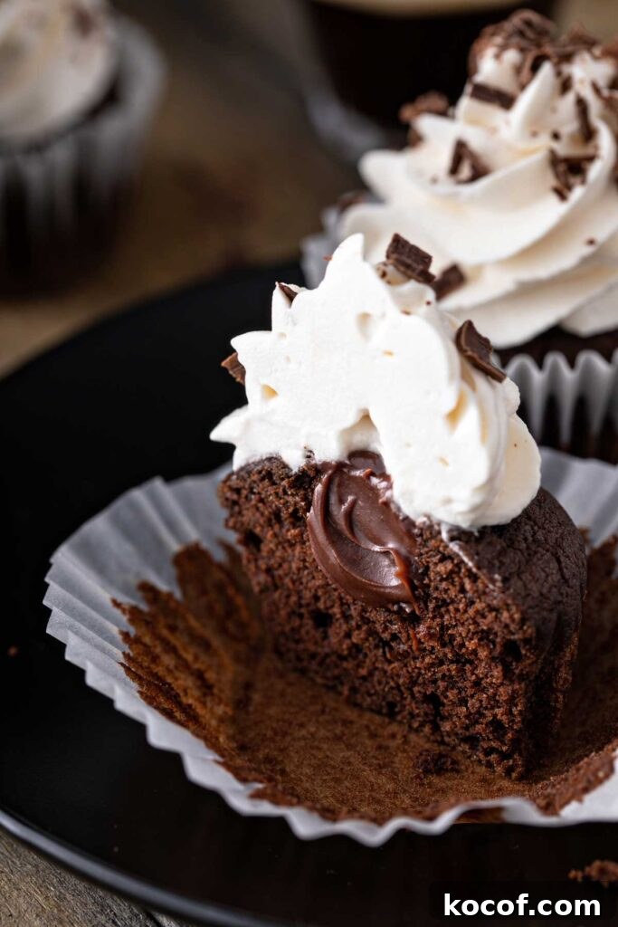 Moist Guinness chocolate cupcake with whipped frosting, cut in half showing it's ganache filling