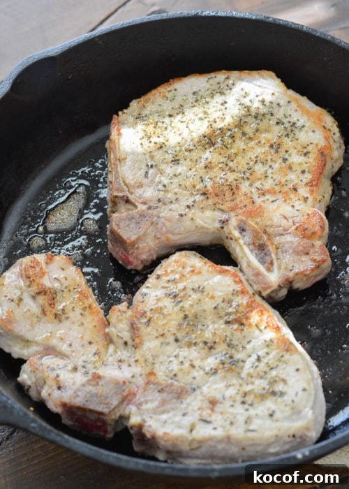 Creamy One-Pan Pork Chops with Garlic Herb Sauce 4 bone-in pork chops searing in a cast iron skillet with olive oil