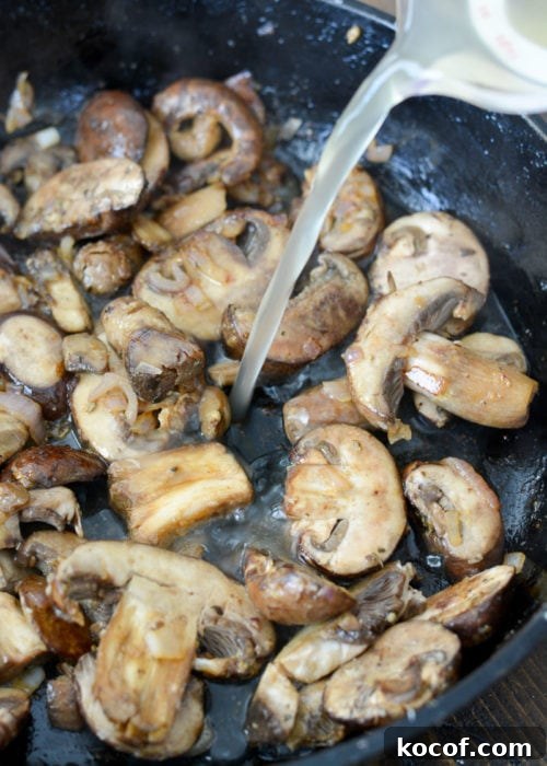 Creamy One-Pan Pork Chops with Garlic Herb Sauce 7 chicken broth and white wine being poured into a cast iron skillet with sauteed mushrooms, shallots, and garlic