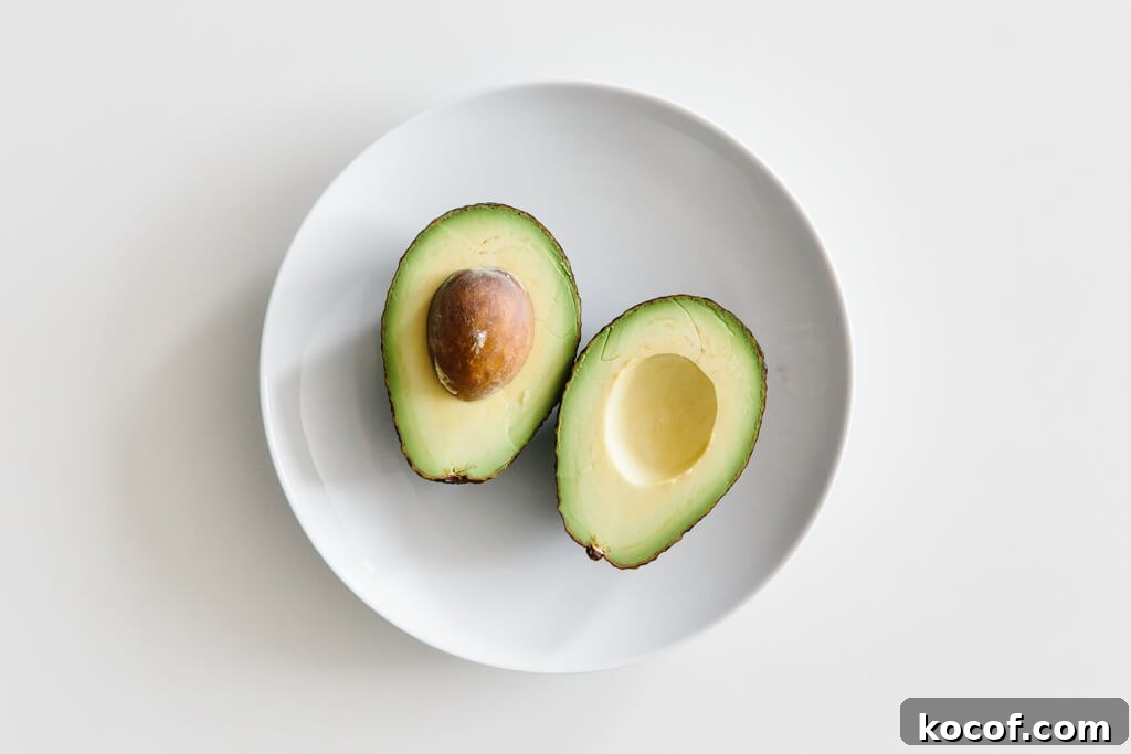 Plate of avocado sliced in half on a white table.