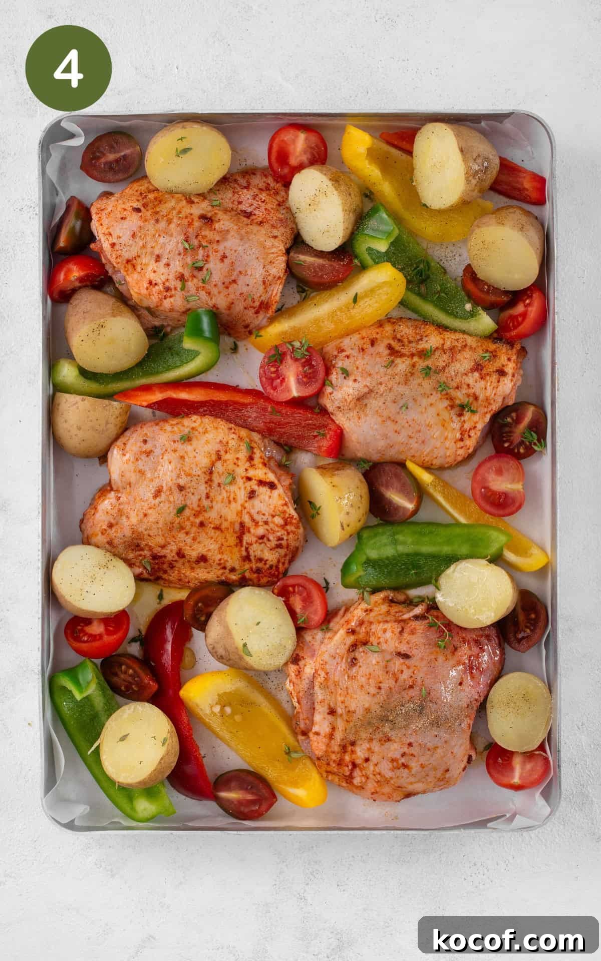 Crispy Herb-Roasted Chicken Thigh Tray Bake with Vegetables 7 Vegetables and chicken thighs on a baking tray.