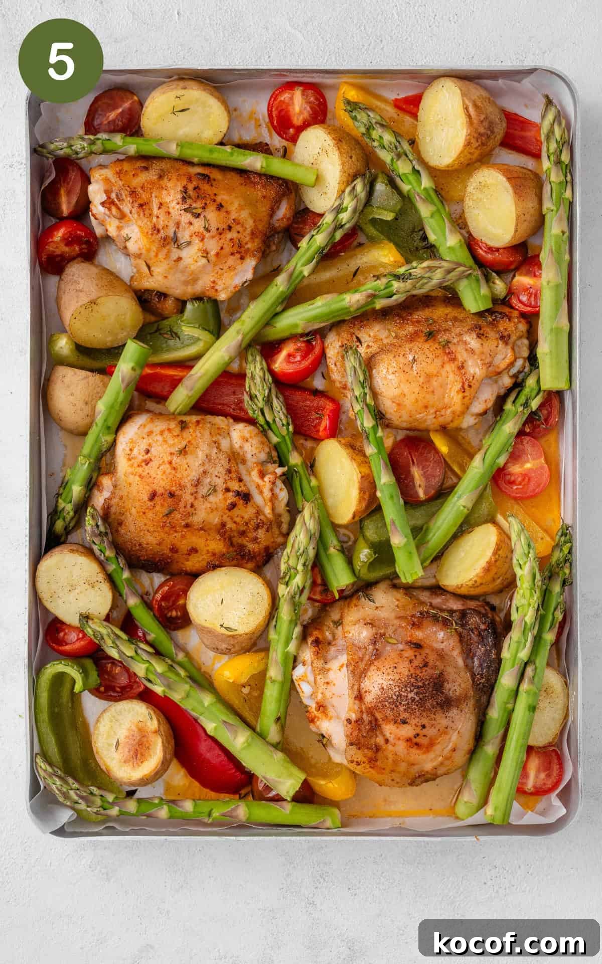 Crispy Herb-Roasted Chicken Thigh Tray Bake with Vegetables 8 Chicken thighs, asparagus and other vegetables on a baking tray.