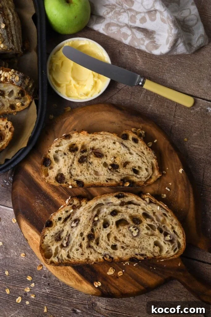 2 slices of sourdough apple crisp bread laid on a round wooden board so you can see the crumb inside. Around the slices of bread you can see a dish of butter, a floral dish towel and a green apple.