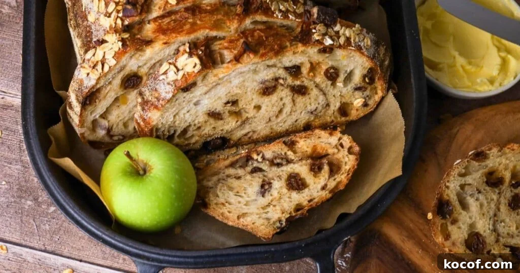 Sourdough apple crisp loaf sliced open so you can see the inside. The loaf is displayed inside a cast iron bread pan with a green apple next to it.