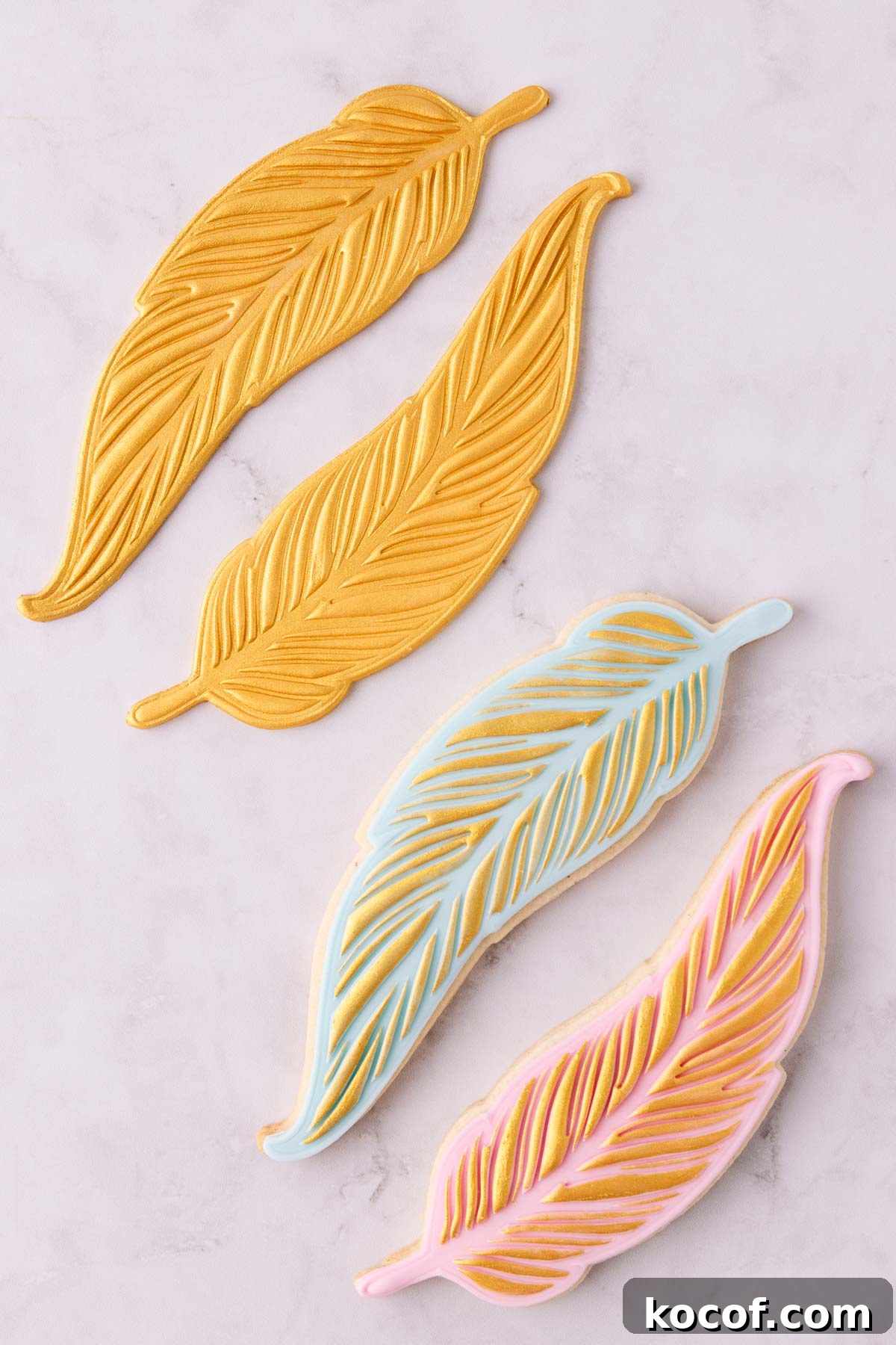 Make Edible Gold Paint at Home: A Step-by-Step Guide 15 Two gold painted feather fondant shapes and two cookies, one with pink fondant and one with light blue fondant, both with gold painted details.