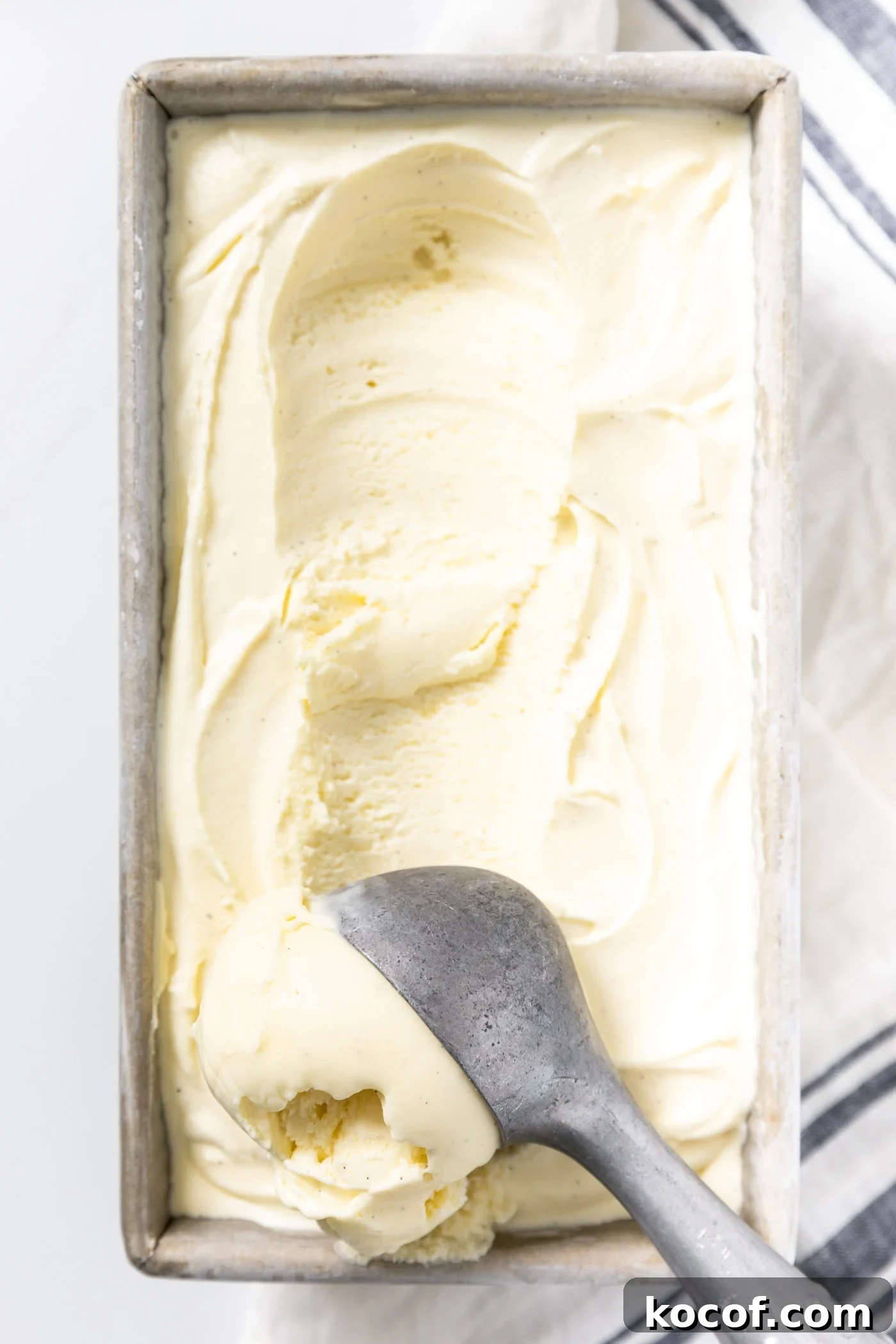 Close up view of ice cream scoop scooping vanilla ice cream from silver container in which it was frozen