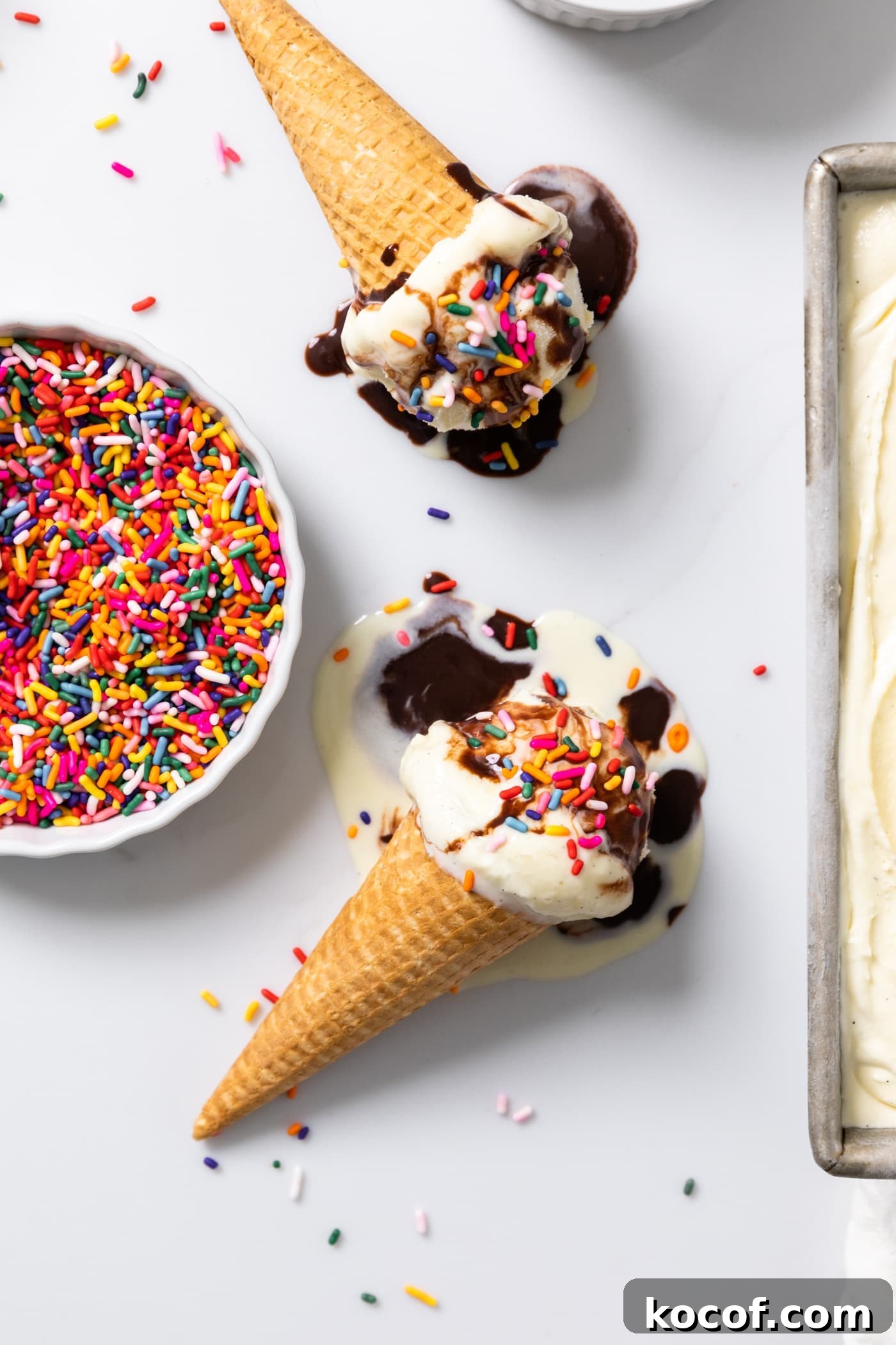 Top down view of vanilla ice cream sitting in ice cream cones with fudge and sprinkles all over the top