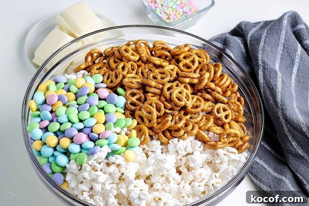 Bunny Bait Easter Snack Mix — No-Bake Party Treat 4 Clear glass bowl filled with popcorn, pretzel and candies with gray napkin.